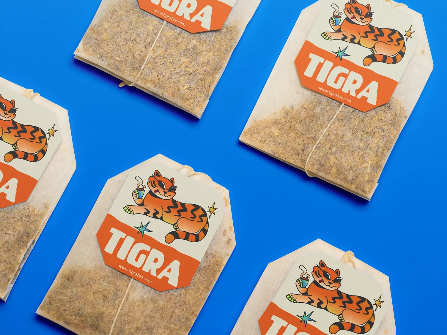 Čajové sáčky TIGRA s oranžovými štítky a ilustrovaným tygrem na modrém pozadí